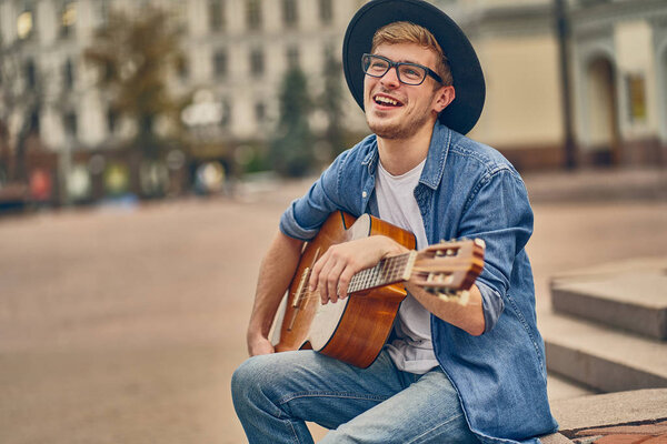 Young man playing the guitar. Stylish hipster guy with hat enjoy