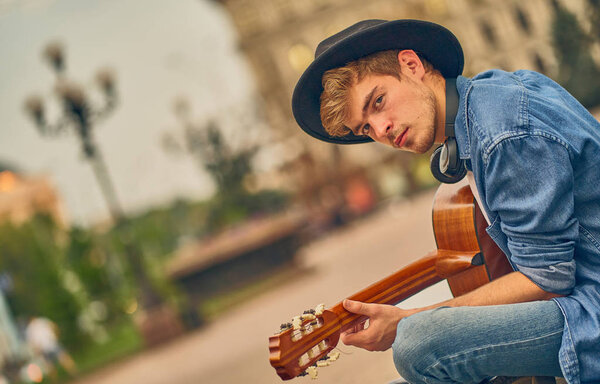 Молодой человек играет на гитаре. Стильный парень-хипстер наслаждается музыкой
