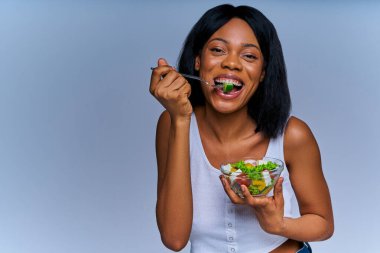 Beyaz bluzlu mutlu kız cam kaseden karışık salata yiyor.