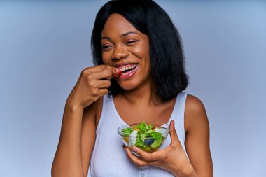 Beyaz bluzlu neşeli bayan cam tabaktan taze kırmızı sebze yiyor.