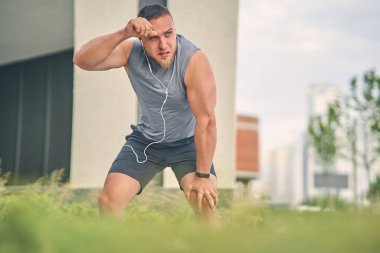 Uzun sakallı kaslı bir adam sokakta dururken alnından terini siliyor..