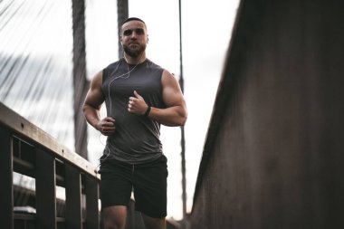 Ufuk çizgisini tıkayan fotoğrafta, hafif spor giyimli kaslı bir adam akşam koşusunda..