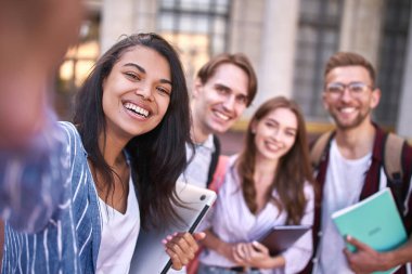 Ellerinde not defterleri olan iki kız ve iki erkek fotoğraf çekimi için kameraya gülümsüyor..