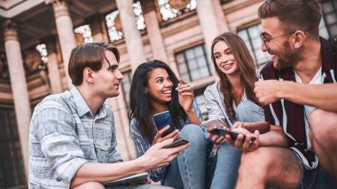 Elinde telefonlar olan bir grup gürültücü genç müzenin yanında oturuyorlar..