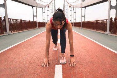 Açık havada köprüde kalırken koşudan önce kablosuz kulaklık takan formda atletik bir kadın. Sağlık ve spor konsepti