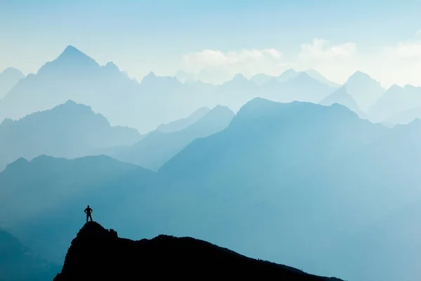 L'uomo raggiunge la cima dopo l'arrampicata e l'escursionismo godendo di libertà e guardando verso le montagne silhouette panorama nelle prime ore del mattino. — Foto Stock