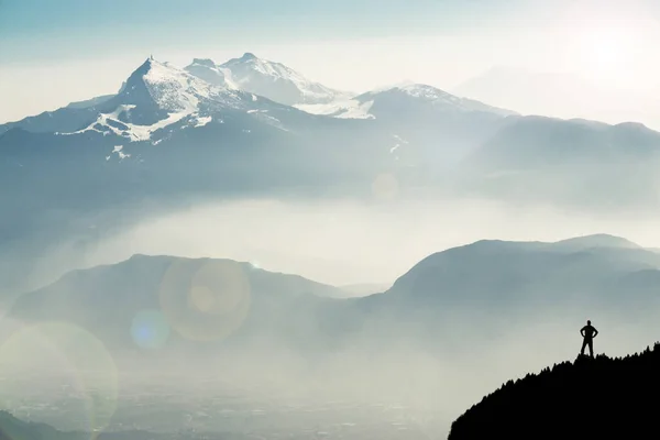 Spectacular mountain ranges silhouettes. Man reaching summit enjoying freedom. View from Top of Mount Corno di Tres, Tresner Horn to Cima Paganella. Trentino, South Tyrol, Alps, Italy.