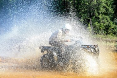 Motokros ATV kullanan bir adam yüksek hızla nehir gölü suyuna doğru sıçrıyor. Foy, Foyross Gölü, Sudbury, Kanada.
