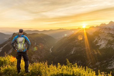 Zirveye ulaşan adam dağlarda inanılmaz gündoğumunun tadını çıkarıyor. Güneş ışığı, güzel lensler ve güneş ışınları. Julian Alps, Triglav Ulusal Parkı, Slovenya, Slemenova Dağı, Sleme.