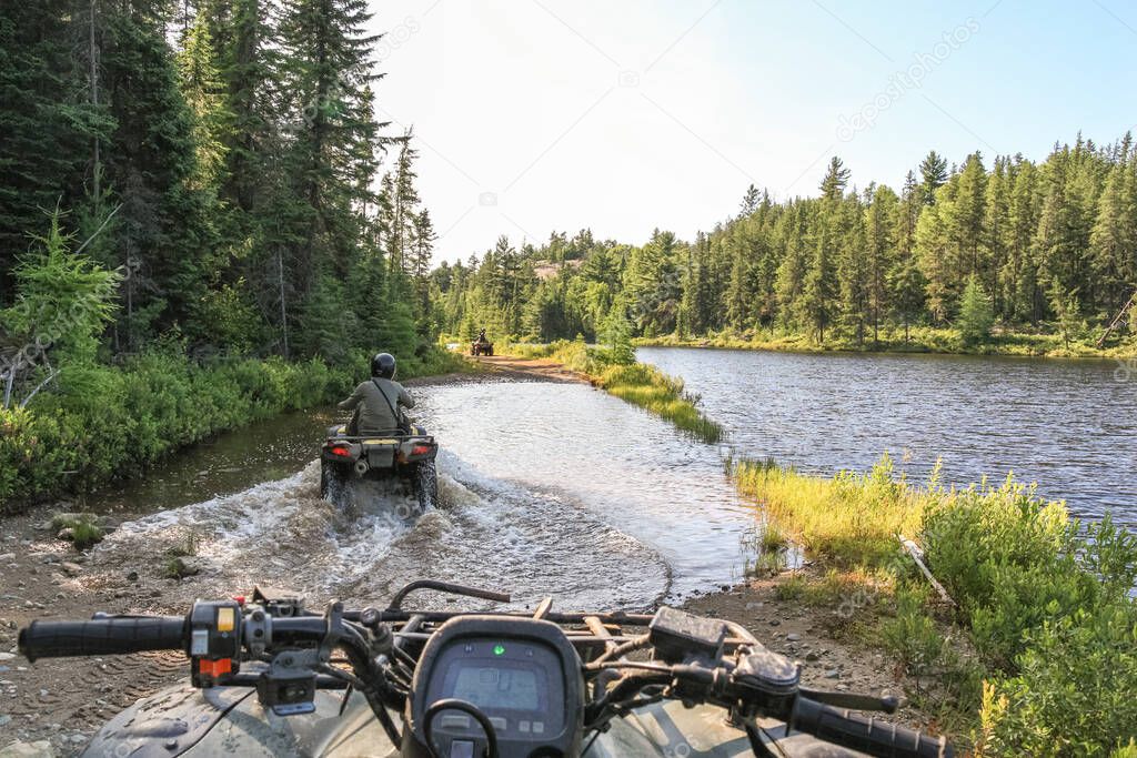 People driving ATV quadbike through water. Lake in Ontario, Canada.
