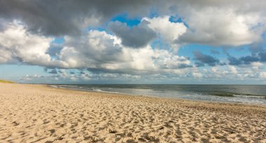 Plaj kumları mavi gökyüzü ve sahil şeridinde dramatik bulutlar yumuşak akşam günbatımında. Hvidbjerg Strand, Blavand, Kuzey Denizi, Danimarka.