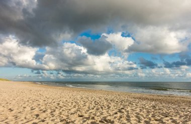 Plaj kumları mavi gökyüzü ve sahil şeridinde dramatik bulutlar yumuşak akşam günbatımında. Hvidbjerg Strand, Blavand, Kuzey Denizi, Danimarka.