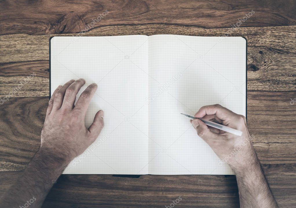 top view of man holding pen to write in diary or notepad on wooden table