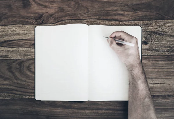 Ovanifrån om man håller pennan att skriva i dagboken eller anteckningar på träbord — Stockfoto