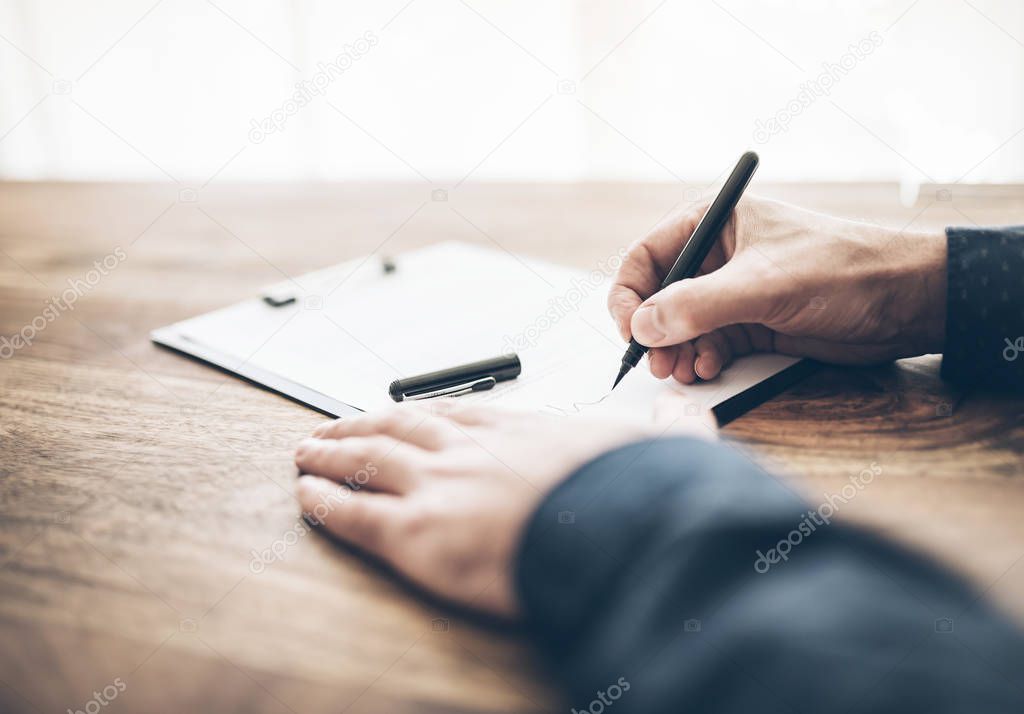 close-up of businessman signing contract or document on wooden desk