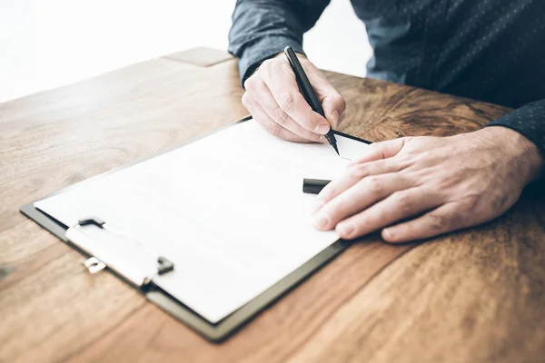 Primer plano del hombre de negocios que firma contrato o documento en escritorio de madera — Foto de Stock