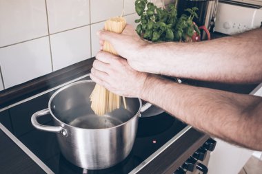 spagetti ile kaynar su ocakta tencerede koyarak eller