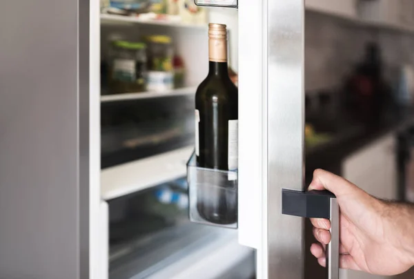 Рука людини, що відкриває двері холодильника на домашній кухні — стокове фото