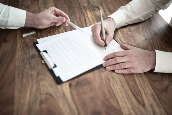 Man undertecknar kontrakt på trä skrivbord med annan person som pekar på dokument — Stockfoto