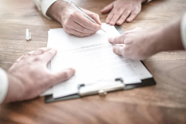 Man undertecknar kontrakt på trä skrivbord med annan person som pekar på dokument — Stockfoto