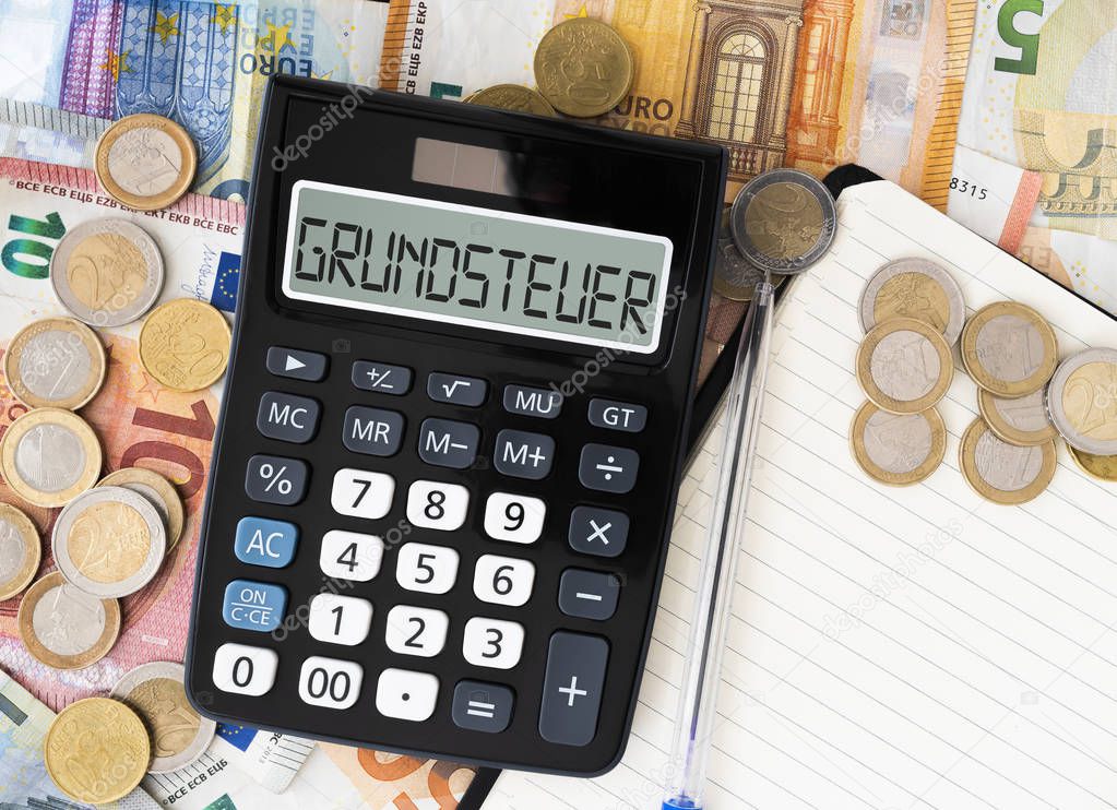 German word Grundsteuer property tax or land tax on display of pocket calculator with euro bills and coins in background