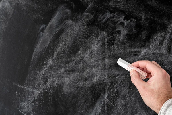 Hand hält Stück Kreide gegen leere staubige Tafel — Stockfoto