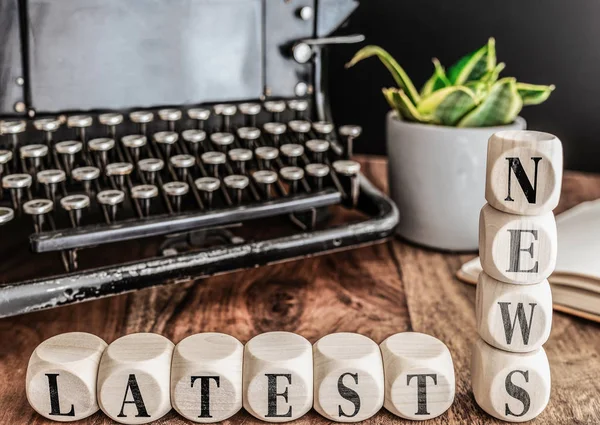 words LATEST NEWS on wooden blocks with vintage typewriter and potted plant in background