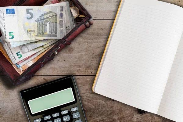 Financiën en huishouding concept met open notitieboek, rekenmachine en houten doos gevuld met contant geld op tafel — Stockfoto