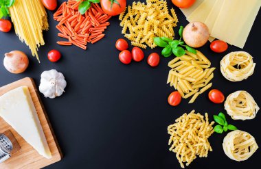 Fesleğenli koyu arka plan üzerinde farklı İtalyan makarna erişte yaprakları, taze domates, soğan, kaşar peyniri ve rende