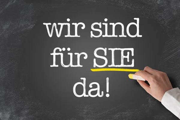 Текст Wir sind хутро Sie Da, німецька для нас тут, щоб допомогти вам, написані на дошці — стокове фото