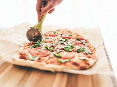 bir pizza kesici kullanarak domates ve fesleğen ile lezzetli ev yapımı pizza Margherita kesme