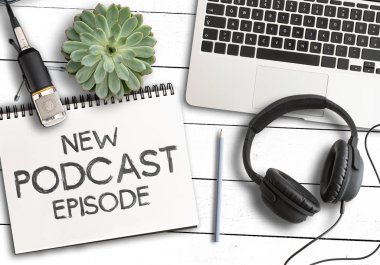 dizüstü bilgisayar, saksı bitki ve beyaz ahşap masa üzerinde kayıt mikrofonu ile not defterinde metin Yeni Podcast Episode