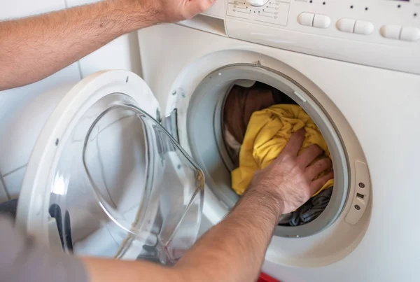Adam renkli giysileri çamaşır makinesine yüklüyor. — Stok fotoğraf