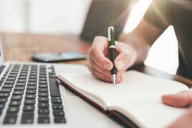 Dizüstü bilgisayarın önünde kalemle not alan kişi