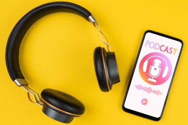 Sarı arka planda canlı yayın yapan akıllı telefon ve kulaklıkların üstü.