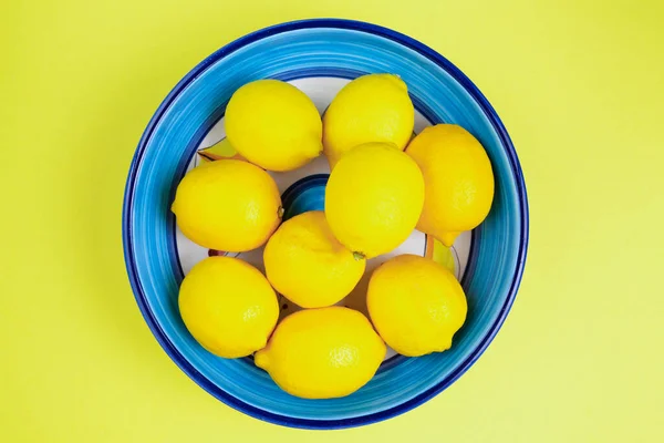 Limões maduros em tigela de cerâmica azul no fundo amarelo — Fotografia de Stock