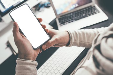 Ofis masasında beyaz dokunmatik ekranlı akıllı telefonu tutan kişi