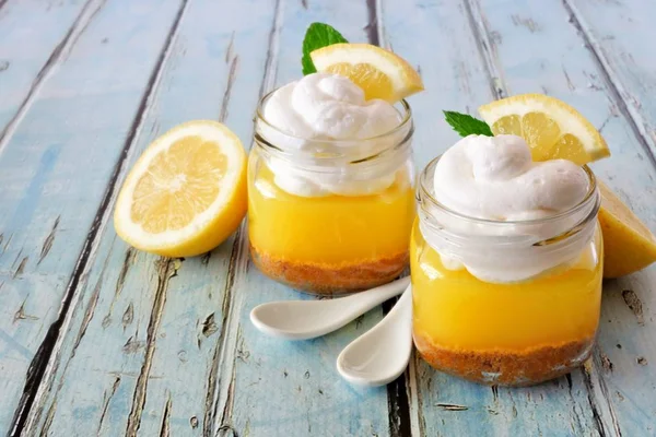Homemade lemon pie in jars with whipped cream against a blue wood background