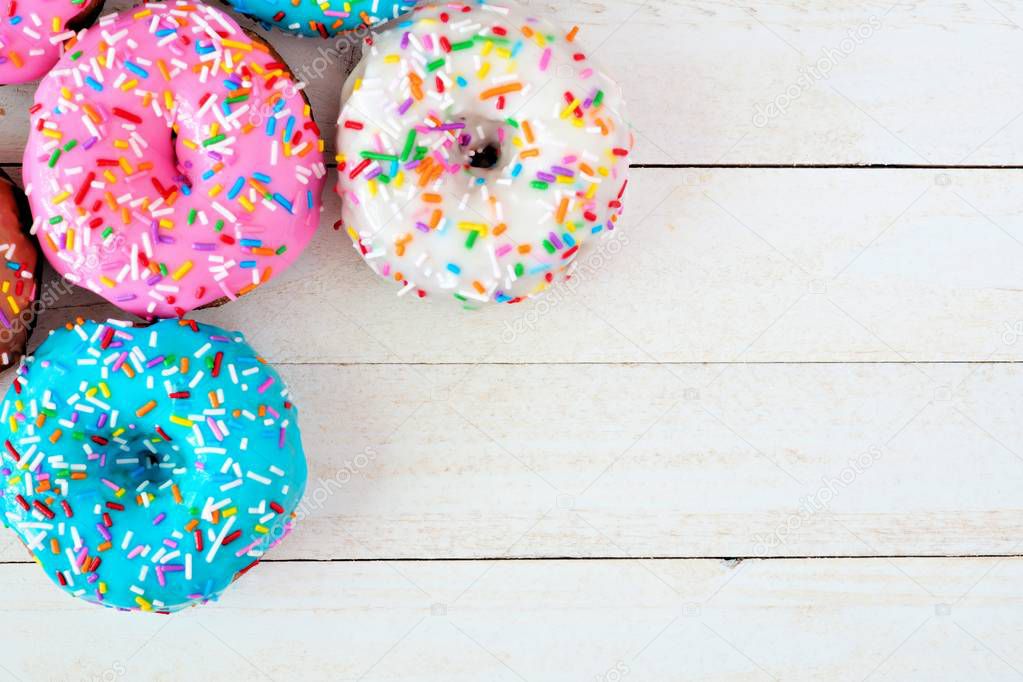 Corner border of assorted donuts with pastel colored icing and sprinkles against a white wood background