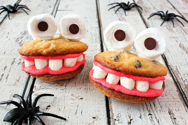 Two Halloween monster cookies with spiders on a rustic white wood background