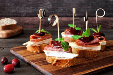 Tatil crostini şişleri kızılcık sosu, brie, salam ve nane ahşap bir sunucu üzerinde