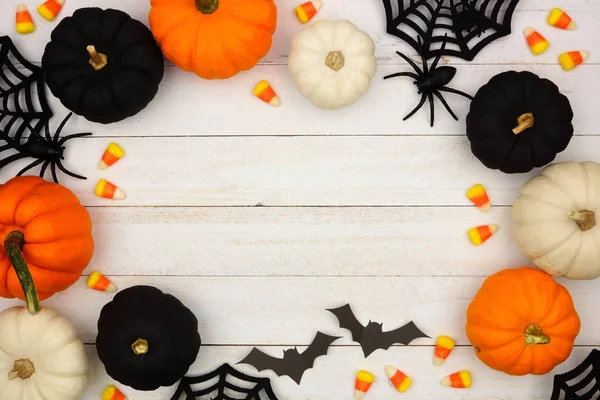 Halloween frame with black, orange and white decor and candy over a white wood background. Top view with copy space.