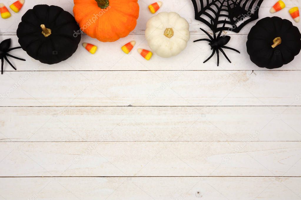 Halloween top border with black, orange and white decor and candy over a white wood background. Top view with copy space.