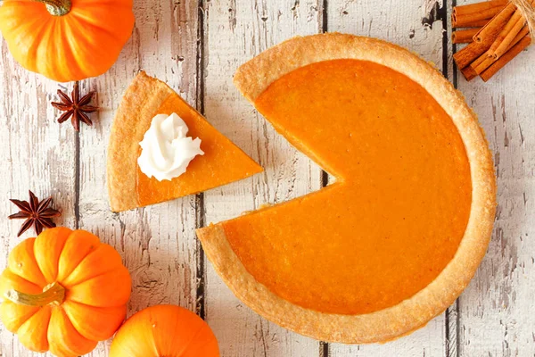 Pumpkin pie with slice removed.  Top view table scene on a rustic white wood background.