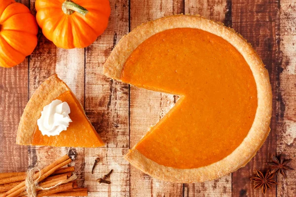 Pumpkin pie with slice removed. Top view table scene on a rustic wood background.