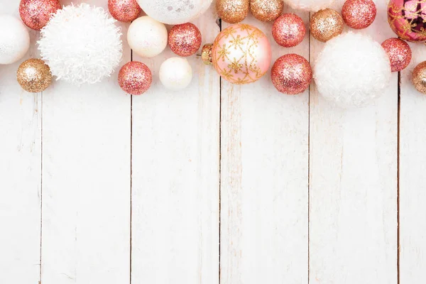 Christmas top border of rose gold, white and gold ornaments on a white wood background