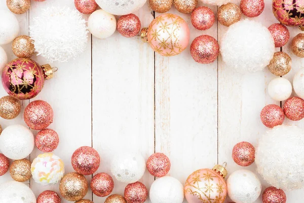 Christmas frame of rose gold, white and gold ornaments on a white wood background