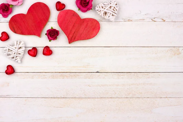 Valentines Day top corner border of hearts, flowers and decor against a rustic white wood background. Copy space.