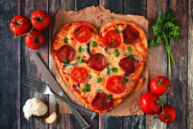 Kalp koyu ahşap arka plan üzerinde Sevgililer günü için pizza şeklinde. Üstten görünüm, tablo sahne malzemelerle.