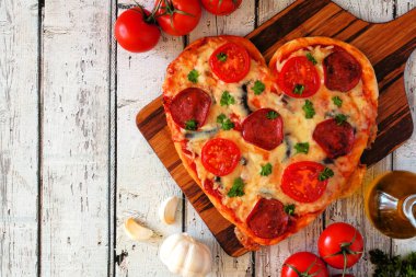 Kalp, Sevgililer günü için bir beyaz tahta arka plan üzerinde pizza şeklinde. Üstten görünüm, yan sınır. Tablo sahne malzemelerle.